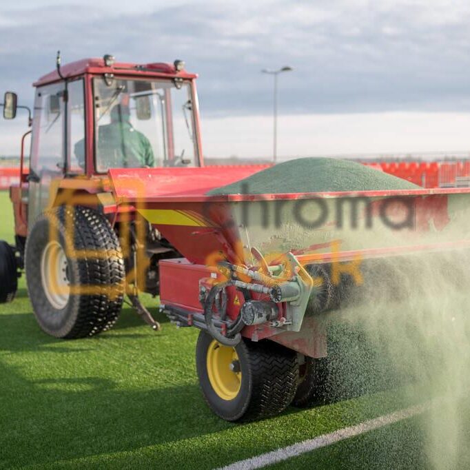 Pouring infill granules in to a football pitch with artificial grass.